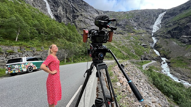 Ei kvinne står ved eit filmkamera og ser ut over fjellandskapet.