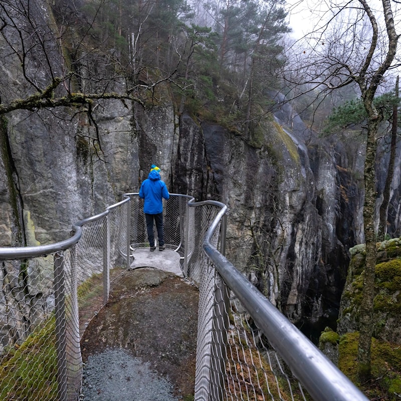 En mann står på et utsiktspunkt og speider ut over Brattlandsddalen.